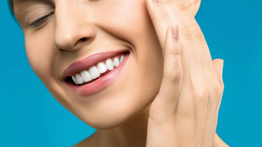 Smiling woman with bright white teeth touching her face, representing cosmetic dentistry results